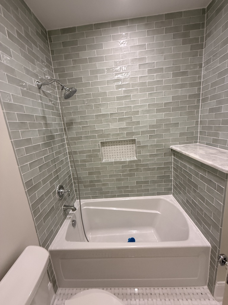 On Track bathroom tile work: green subway tile tub surround with recessed mosaic niche